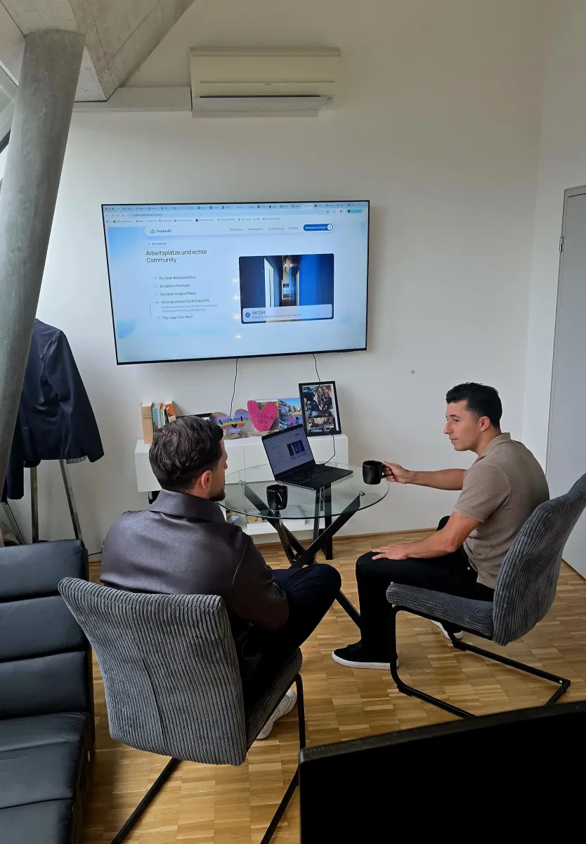 Zwei Personen besprechen sich am Tisch vor dem grossen Screen